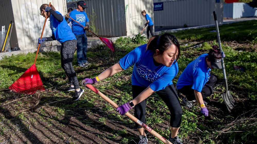 Comcast Cares Day volunteers rake a garden bed.